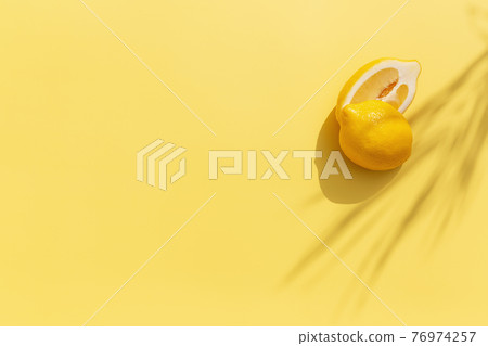 Two halved cuts of lemon with shadow from palm leaf on yellow background Two halved cuts of lemon with shadow from palm leaf on yellow background 76974257