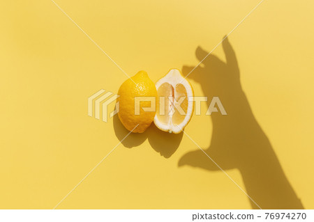Two halved cuts of lemon with shadow from hand on yellow background 76974270