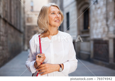 Elegant mature woman is posing in time walking on the street of old city Elegant mature woman is posing in time walking on the street of old city 76974942