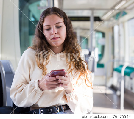 Focused girl on public transport, texting on mobile phone Focused girl on public transport, texting on mobile phone 76975544