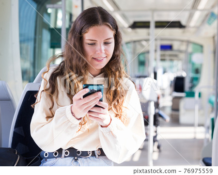 Young woman using smart phone while traveling in tram 76975559
