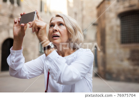 Mature woman is taking photos on her camera while journey through the city 76975704