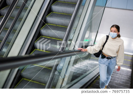 Young girl in protective face mask, standing on the escalator Young girl in protective face mask, standing on the escalator 76975735