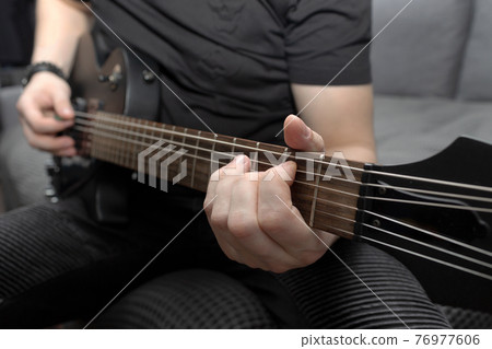 Musician playing black electric guitar. Guitar fretboard close-up. Learning to play the guitar. Self-development at home Musician playing black electric guitar. Guitar fretboard close-up. Learning to play the guitar. Self-development at home 76977606