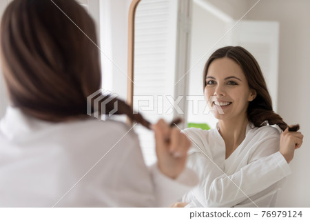 Happy young woman in bathrobe pulling tuft of hair Happy young woman in bathrobe pulling tuft of hair 76979124
