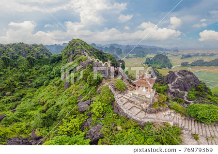Family of tourists on the background of Amazing huge dragon statue at limestone mountain top near Hang Mua view point at foggy morning. Popular tourist attraction at Tam Coc, Ninh Binh. Vietnam travel Family of tourists on the background of Amazing huge dragon statue at limestone mountain top near Hang Mua view point at foggy morning. Popular tourist attraction at Tam Coc, Ninh Binh. Vietnam travel 76979369