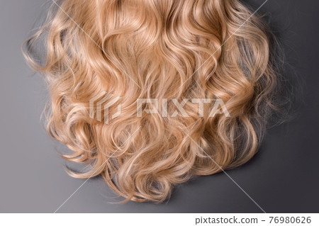 Blonde hair texture. Wavy long curly blond hair close up as background. Hair extensions, materials and cosmetics, wig, hair care. Hairstyle, haircut or dying in salon. 76980626