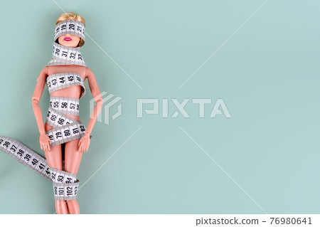 Doll wrapped in measuring tape. Tied up unrecognizable plastic doll, weight loss, fasting and slimming, diet, anorexia, overeating control, female fight for perfect fit body concept. Free copyspace Doll wrapped in measuring tape. Tied up unrecognizable plastic doll, weight loss, fasting and slimming, diet, anorexia, overeating control, female fight for perfect fit body concept. Free copyspace 76980641