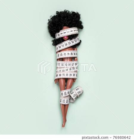 Doll wrapped in measuring tape. Tied up unrecognizable plastic doll, weight loss, fasting and slimming, diet, anorexia, overeating control, female fight for perfect fit body concept. Doll wrapped in measuring tape. Tied up unrecognizable plastic doll, weight loss, fasting and slimming, diet, anorexia, overeating control, female fight for perfect fit body concept. 76980642
