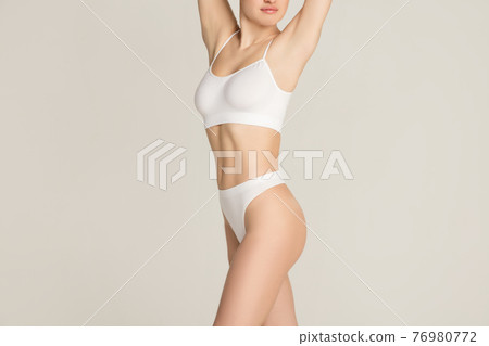Cropped slim tanned beautiful woman in underwear isolated over gray background. Cropped slim tanned beautiful woman in underwear isolated over gray background. 76980772