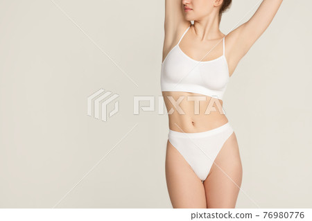 Cropped slim tanned beautiful woman in underwear isolated over gray background. Cropped slim tanned beautiful woman in underwear isolated over gray background. 76980776