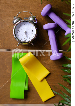 Alarm clock and women dumbbells lying on wooden table. Alarm clock and women dumbbells lying on wooden table. 76982617