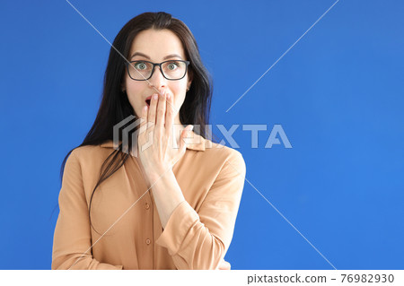 Surprised woman with glasses covers her mouth with her hand 76982930