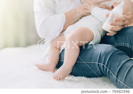 Caring mother bottle feeds her newborn baby. Caring for the health of children. Artificial feeding of children Caring mother bottle feeds her newborn baby. Caring for the health of children. Artificial feeding of children 76982996