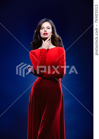 Portrait of pretty feminine woman with earrings, red lipstick and dress on dark background.  76985013
