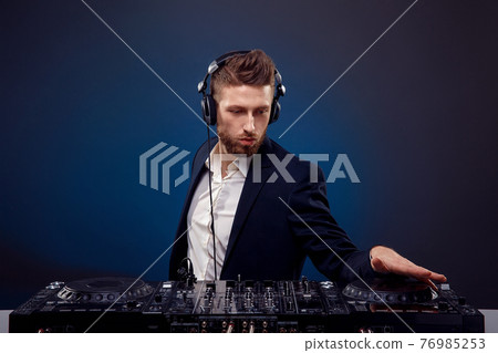 Man DJ in dark suit play music on a Dj's mixer. Studio shot. Dark blue background 76985253