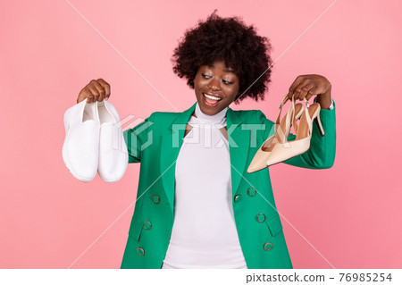 African Lady Holding Sneakers And High-Heels Choosing Shoes, Pink Background African Lady Holding Sneakers And High-Heels Choosing Shoes, Pink Background 76985254