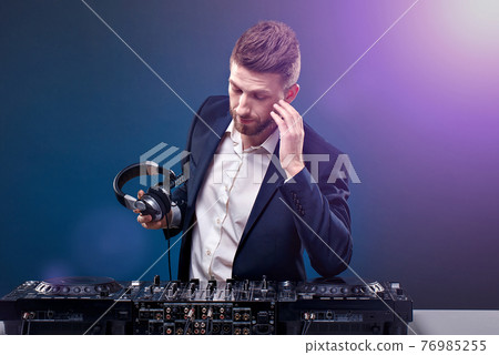 Man DJ in dark suit play music on a Dj's mixer. Studio shot. Dark blue background 76985255