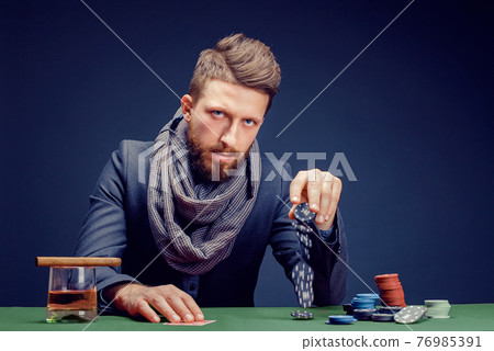 Stylish bearded Man in suit and scarf playing in dark casino, smoking cigar, drink whiskey Stylish bearded Man in suit and scarf playing in dark casino, smoking cigar, drink whiskey 76985391