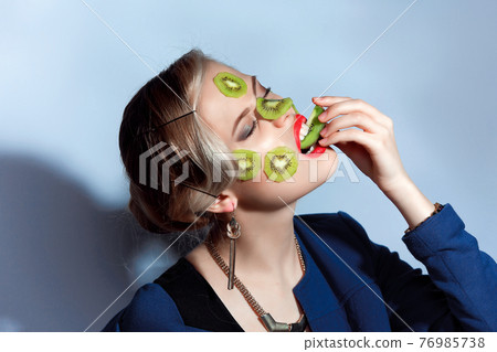 Fashion photo of woman posing with slices of kiwi on her face Fashion photo of woman posing with slices of kiwi on her face 76985738