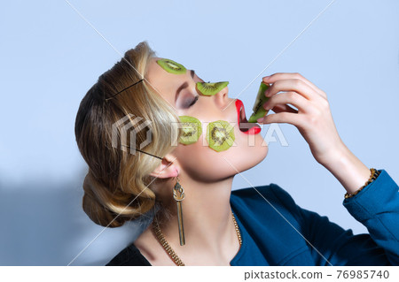 Fashion photo of woman posing with slices of kiwi on her face 76985740