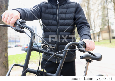 Man holding wheel of bicycle outdoors closeup Man holding wheel of bicycle outdoors closeup 76986981