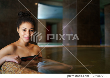 Portrait of young woman in indoor hot spring thermal pool, looking at camera. Portrait of young woman in indoor hot spring thermal pool, looking at camera. 76987209