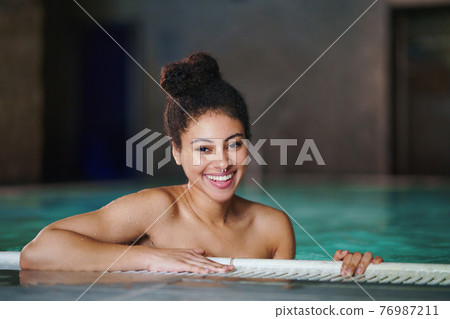 Portrait of young woman in indoor swimming pool, looking at camera. Portrait of young woman in indoor swimming pool, looking at camera. 76987211