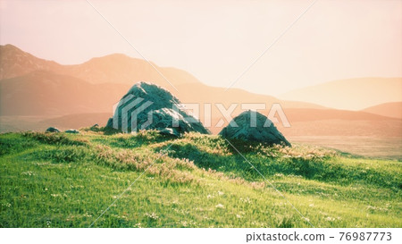 meadow with huge stones among the grass on the hillside at sunset 76987773