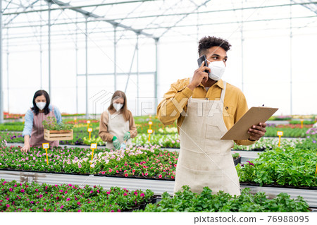 People working in greenhouse in garden center, coronavirus concept. People working in greenhouse in garden center, coronavirus concept. 76988095