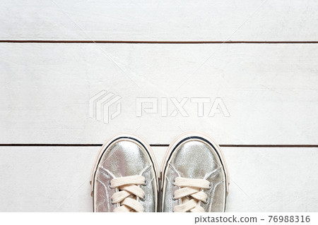 child metallic silver sneakers on white wood board background texture with copy space. White sneakers for girls. Top view 76988316