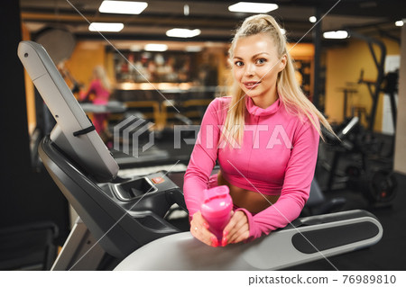 Young healthy blonde woman on a treadmill holding bottle of water at the gym. 76989810