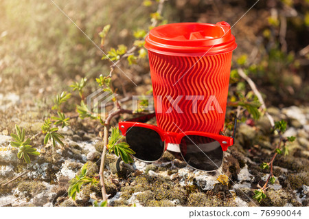 red cardboard glass for coffee and sunglasses with red rim, outdoors, against the background of fresh greenery, concept - summer and picnic in nature red cardboard glass for coffee and sunglasses with red rim, outdoors, against the background of fresh greenery, concept - summer and picnic in nature 76990044