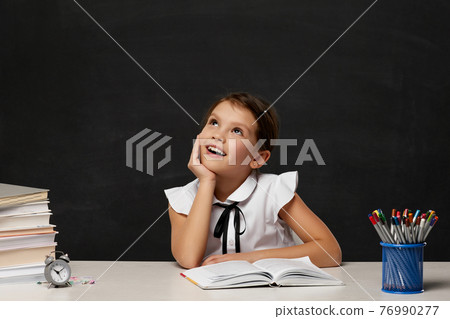 happy schoolgirl daydreaming and sitting at table 76990277