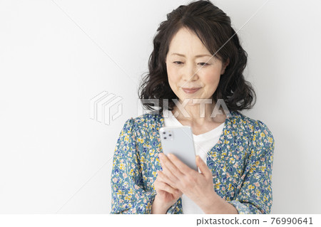 A smiling woman in her 60s looking at the screen of her smartphone 76990641