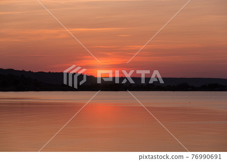 orange sunset, the sun went behind the coastline, the sky is illuminated by the sun, a beautiful sky with orange clouds, a reflection of the sky in the water, the landscape 76990691