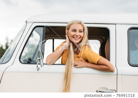 Happy woman with long hair looks out of car window while sitting on driver seat Happy woman with long hair looks out of car window while sitting on driver seat 76991318