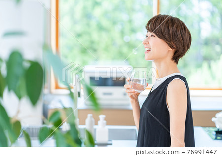 A woman hydrating in the kitchen. 76991447