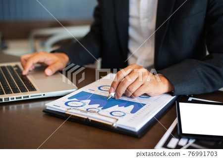 Businessman using digital laptop analyzes business data, busy working on tablet and business report on office desk, business strategy analysis concept. Businessman using digital laptop analyzes business data, busy working on tablet and business report on office desk, business strategy analysis concept. 76991703