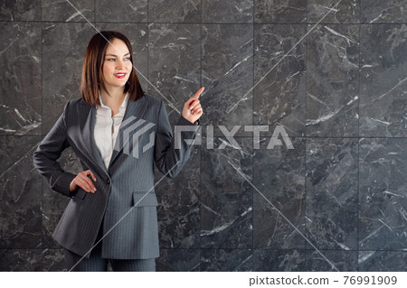 Young brunette in business gray suit, points to copy space 76991909