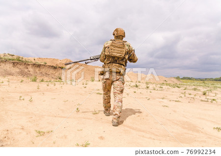 Soldier in camouflage with rifle walks across desert 76992234