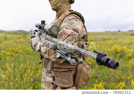 Soldier with rifle standing in green field 76992312