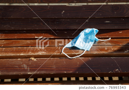 Photo of throwed used protective mask on the wooden bench 76993343