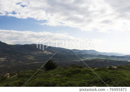 A view of a mountain range and a green valley in the morning at sunrise, against a dramatic back of blue skies and clouds. High quality photo. Travel concept hiking. North District Israel A view of a mountain range and a green valley in the morning at sunrise, against a dramatic back of blue skies and clouds. High quality photo. Travel concept hiking. North District Israel 76995871