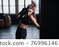 Athletic fit female boxer exercising punches with boxing bag in gym during kickboxing and self defense intensive workout 76996146