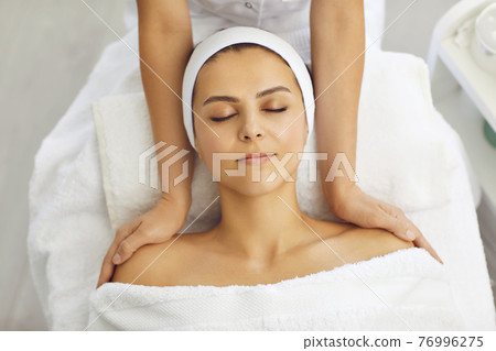 Cosmetologist making massage of face, neck and upper shoulder girdle for relaxed young woman in beauty spa salon Cosmetologist making massage of face, neck and upper shoulder girdle for relaxed young woman in beauty spa salon 76996275