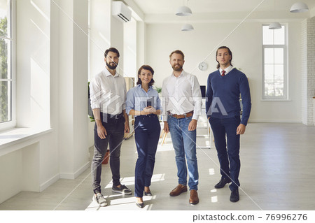 smiling business partners or project team standing and looking at camera in modern office 76996276