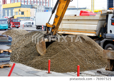 A road excavator bucket collects crushed sand to load it onto a truck. A road excavator bucket collects crushed sand to load it onto a truck. 76997325