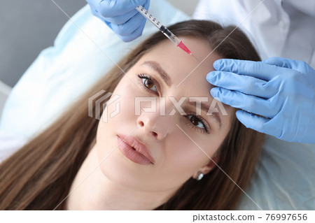 Portrait of woman whose beautician makes injection of botulinum toxin in forehead Portrait of woman whose beautician makes injection of botulinum toxin in forehead 76997656