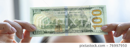 Woman holding dollar bill and looking at it with watermarks closeup 76997950